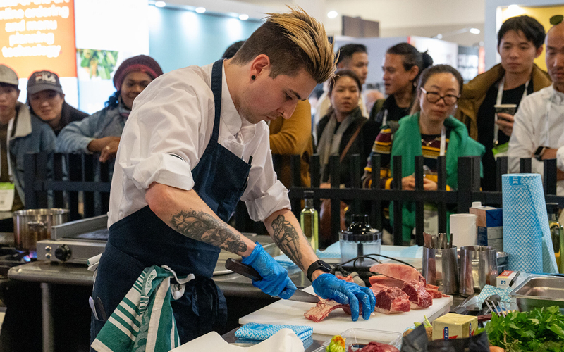 Chef with tattoos cutting meat on a white cutting board at a chef of the year
