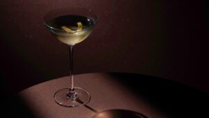 A chilled martini served in a coupe glass with a lemon twist, spotlighted on a dark, moody background.