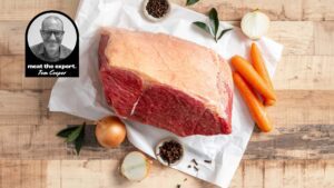 Raw corned beef silverside on butcher’s paper with carrots, onions, bay leaves, cloves and peppercorns, alongside a portrait of meat expert Tom Cooper.