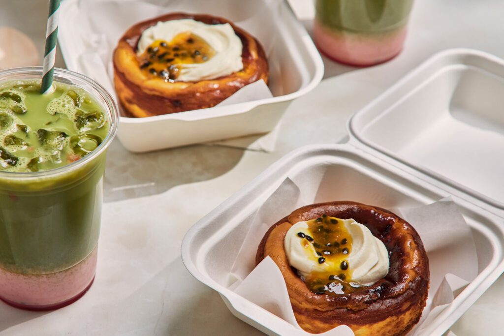 Baked passionfruit and white chocolate cheesecakes in takeaway containers, served with strawberry iced machas to go.