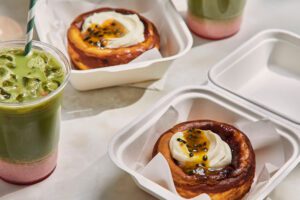 Baked passionfruit and white chocolate cheesecakes in takeaway containers, served with strawberry iced machas to go.