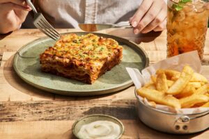 An image of a moody dinner setting. Served is a rich, creamy tomato vodka pasta with tender beef mince, served in a bowl and topped with grated parmesan and fresh basil leaves. The pasta is coated in a velvety sauce, with a hint of vodka adding depth to the flavor.