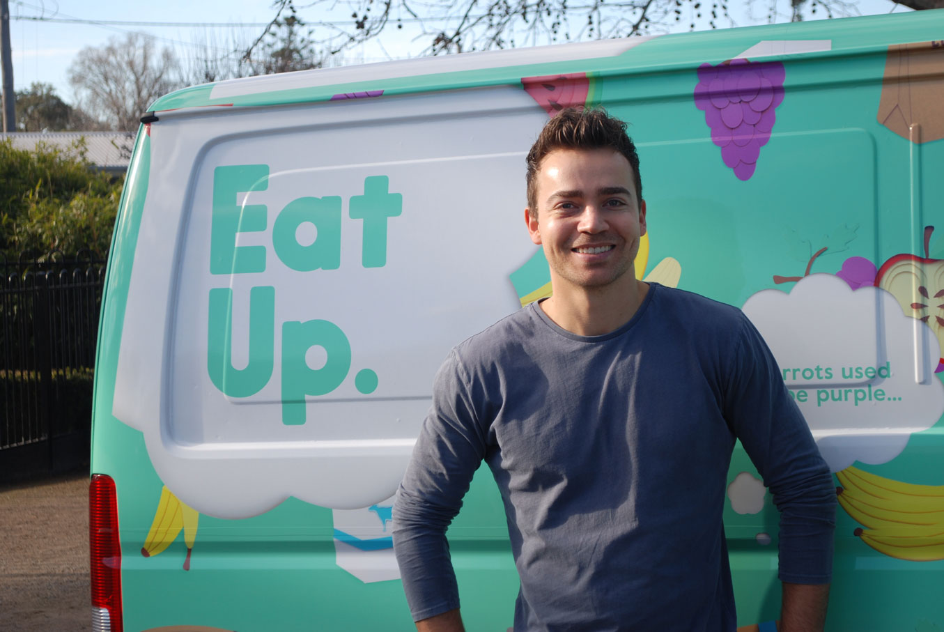 Lyndon Galea standing in front of a colorful Eat Up van featuring illustrations of fruits and vegetables, promoting the healthy eating initiative.