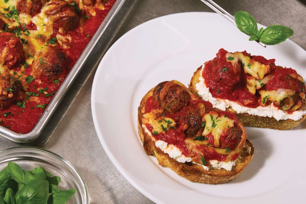 toasted bread topped with ricotta, baked meatballs, and rich tomato sauce, served on a white